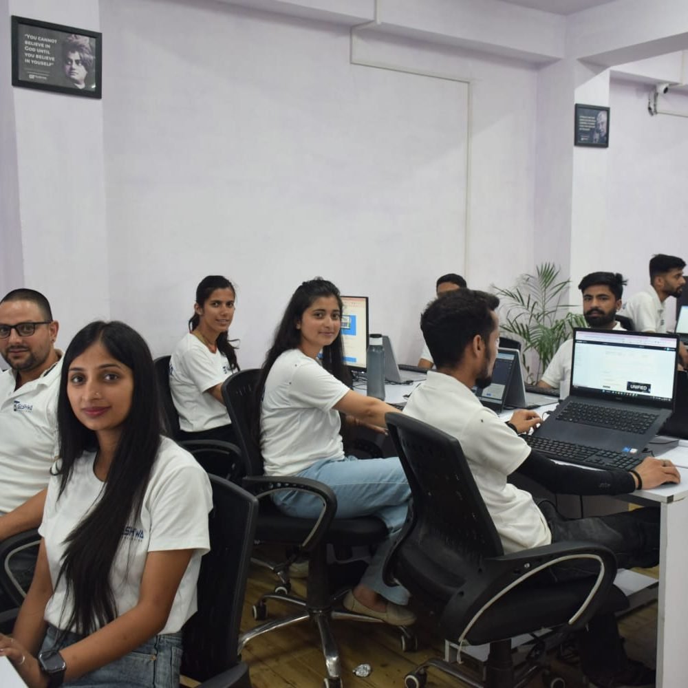 A group of Gashwa Technologies employees working diligently at their desks with computers in a modern office setting.